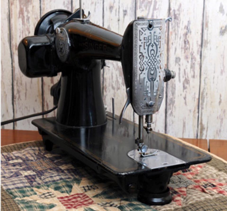 A black Singer sewing machine from the side with the hand wheel, showing the motor.
