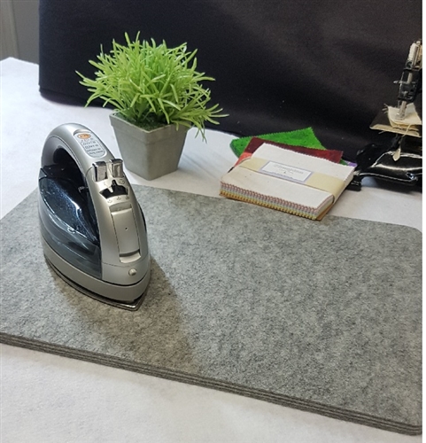 A wool felt mat with a small iron on it, and some decorative objects behind it.