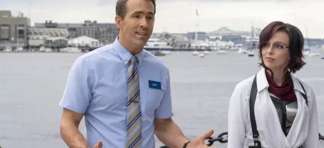 A white man in a blue shirt and tie and a white woman in a white shirt stand in front of a harbor.